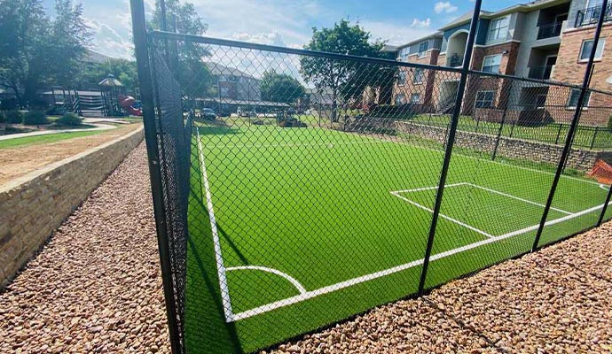 Fenced-in artificial turf sports court at an apartment complex.