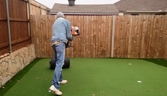 Artificial turf putting green maintenance Worker using a power broom on a backyard putting green.